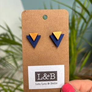 May include: A pair of blue and gold triangle shaped earrings on a brown card with the text "L&B Lou Lou & Belle".