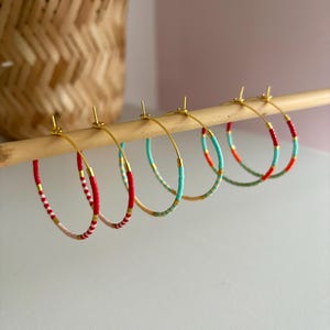 May include: Five pairs of hoop earrings with colourful beaded designs. The hoops are made of gold metal and are decorated with red, white and turquoise beads.