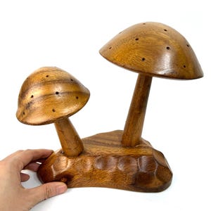 Könnte beinhalten: Eine Holzskulptur in Form eines Pilzes mit zwei Pilzen auf einem Sockel. Die Pilze sind braun und haben Löcher oben. Der Sockel ist ebenfalls braun und hat eine raue Textur.