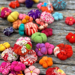 Peut inclure: Une collection de fleurs en tissu colorées, chacune avec un design et une texture uniques. Les fleurs sont faites de différents tissus, dont le coton, la soie et le velours. Elles sont disposées sur une surface en bois.