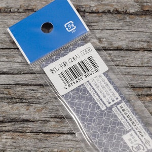 May include: A close-up of a plastic package containing two embroidery needles. The package is labeled "刺し子針 (2本入)" and has a barcode. The text "Needle: Handle Wit" is also visible on the package.