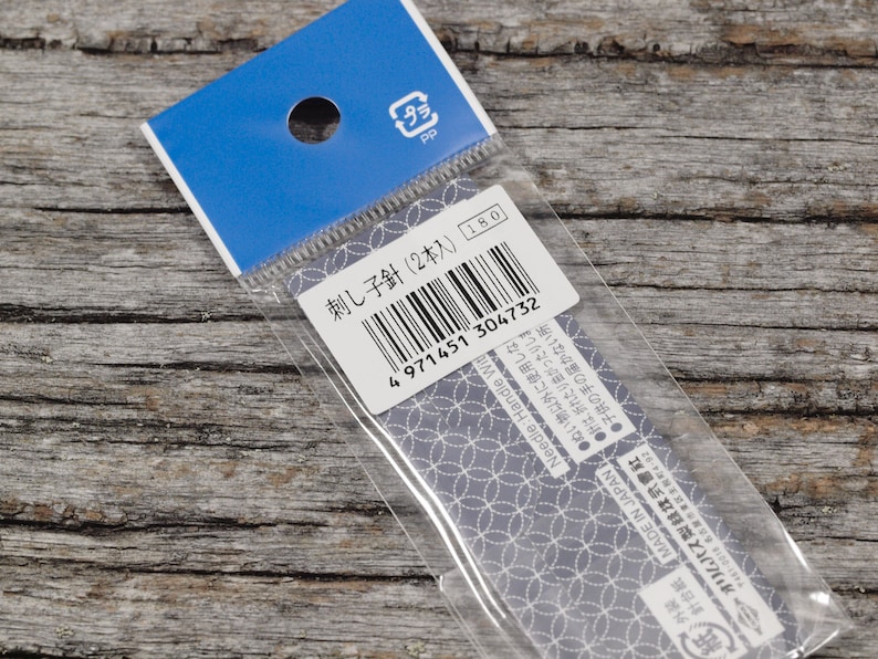 May include: A close-up of a plastic package containing two embroidery needles. The package is labeled "刺し子針 (2本入)" and has a barcode. The text "Needle: Handle Wit" is also visible on the package.