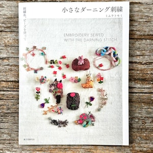 May include: A white book cover titled "小さなダーニング刺繍" and "EMBROIDERY SEWED WITH THE DARNING STITCH." The cover features a collection of colourful, small embroidered motifs, including flowers, a small animal figure, and yarn-based shapes.