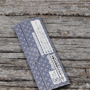 May include: Close-up of a blue and white patterned paper package with Japanese text that reads "MADE IN JAPAN" and "Needle: Handle With Care". The text also includes instructions for use and storage.