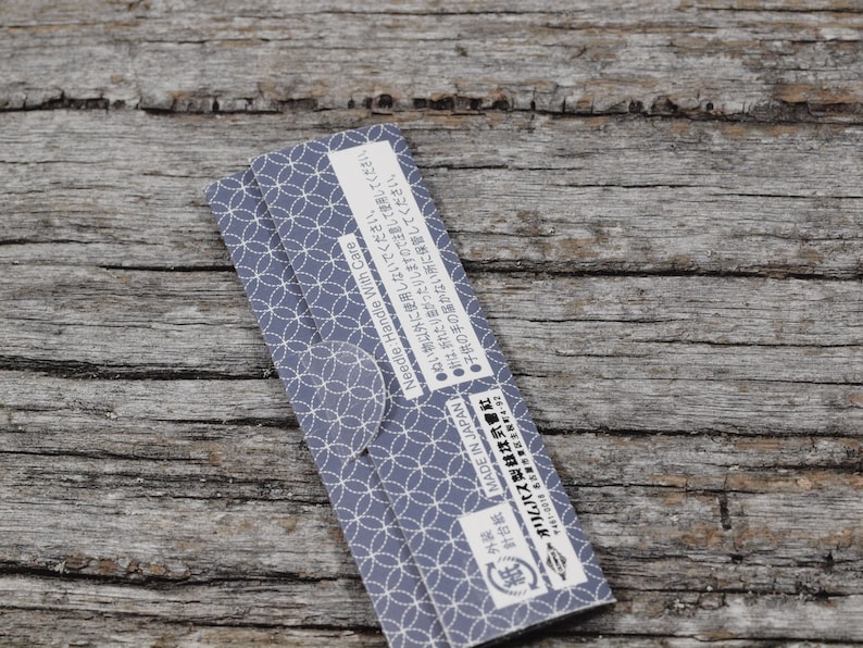May include: Close-up of a blue and white patterned paper package with Japanese text that reads "MADE IN JAPAN" and "Needle: Handle With Care". The text also includes instructions for use and storage.