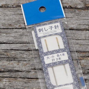 May include: A package of two Sashiko needles, one large and one small. The package is white with blue and gray accents and Japanese text that reads "Sashiko Needle" and "Large: 1 Needle, Small: 2 Needles".