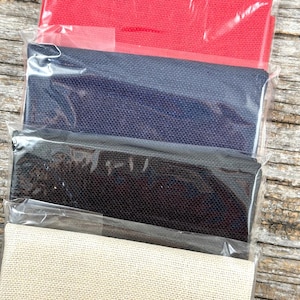 May include: Four rolls of fabric in different colours: red, navy blue, black, and beige. The fabric is wrapped in clear plastic and is ready to be used for crafting projects.