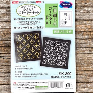 Può includere: Un kit iniziale per ricamo sashiko Olympus per due sottobicchieri, modello SK-300. La confezione presenta testo in giapponese, un codice a barre e immagini di due sottobicchieri quadrati con motivi geometrici gialli e bianchi su tessuto blu scuro, che misurano 10cm per 10cm.