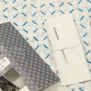 May include: A close-up of a white fabric with blue stitching in a cross pattern. Two silver needles are on a white paper with the text "大・小 各1本 計2本".