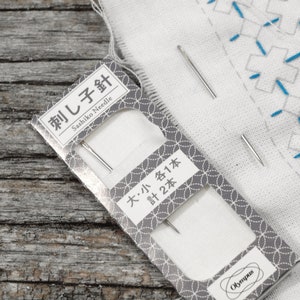 May include: A package of two sashiko needles, labeled "Sashiko Needle" and "大・小 各1本 計2本". The needles are silver and are packaged on a white background with a gray and white pattern.