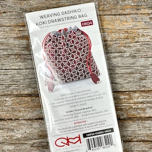 Peut inclure: Un sac à cordon de serrage KOKI avec un motif géométrique bordeaux et blanc, intitulé "WEAVING SASHIKO KOKI DRAWSTRING BAG". Le sac est en 100% coton et mesure environ 35cm x 45cm. L'emballage contient des informations sur l'entretien et l'origine du produit.