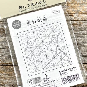 May include: A packaged Sashiko Sampler kit with the text "Hana-Fukin Sashiko Sampler" in English and Japanese. The kit includes a white fabric with a geometric pattern, English instructions, and a finished size of approximately 13.4 x 13.4 inches.