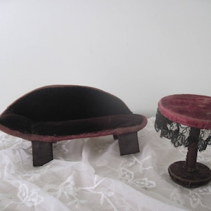 May include: A miniature velvet sofa and side table set. The sofa is a dark burgundy color with a curved back and rests on two rectangular legs. The side table has a burgundy velvet top with black lace trim and a single pedestal base.