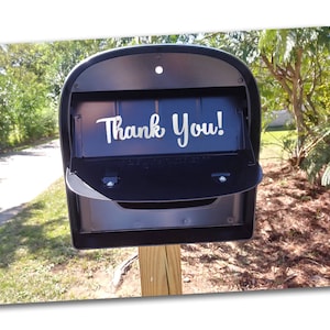 May include: A black mailbox with a white vinyl sticker that says "Thank You!" The mailbox is mounted on a wooden post.