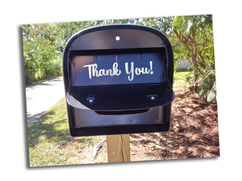 May include: A black mailbox with a white vinyl sticker that says "Thank You!" The mailbox is mounted on a wooden post.
