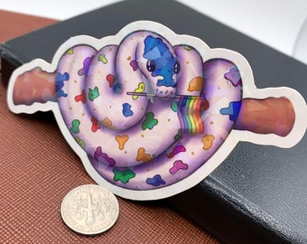 May include: A colorful sticker featuring a cartoon snake with a blue head and a rainbow flag. The snake is white with colorful spots. A dime is next to the sticker.
