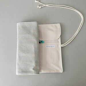 May include: A canvas roll-up case with a striped fabric section and a solid beige pocket. The case is secured with a white cord and a small teal clasp. The text "blissingreen.com" is printed on the pocket.