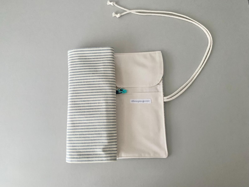 May include: A canvas roll-up case with a striped fabric section and a solid beige pocket. The case is secured with a white cord and a small teal clasp. The text "blissingreen.com" is printed on the pocket.