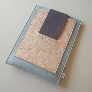 May include: A light blue felt case with a beige felt flap and a black elastic closure. The case has a geometric pattern.