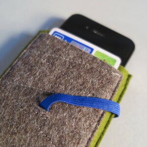 May include: A gray felt phone case with a green felt flap and a blue elastic band. The case has a quilted design and is designed to hold a smartphone.