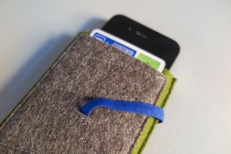May include: A gray felt phone case with a green felt flap and a blue elastic band. The case has a quilted design and is designed to hold a smartphone.