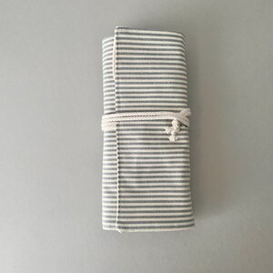 May include: A rolled-up, grey and white striped fabric case, fastened with a white rope. The fabric has a textured feel, and the stripes are horizontal. The design is simple and practical, suitable for various uses.
