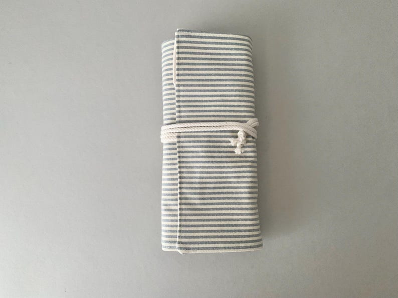 May include: A rolled-up, grey and white striped fabric case, fastened with a white rope. The fabric has a textured feel, and the stripes are horizontal. The design is simple and practical, suitable for various uses.