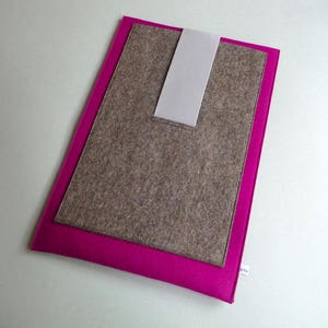 Puede incluir: Una funda para portátil de fieltro rosa con un inserto de fieltro marrón y una correa de fieltro gris.
