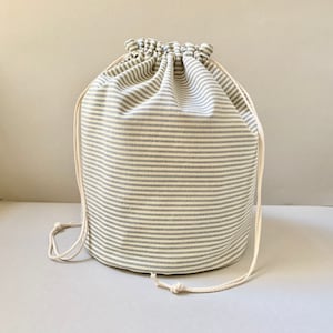 May include: A white drawstring bag with blue stripes. The bag is made of a soft, woven fabric and has a simple design.