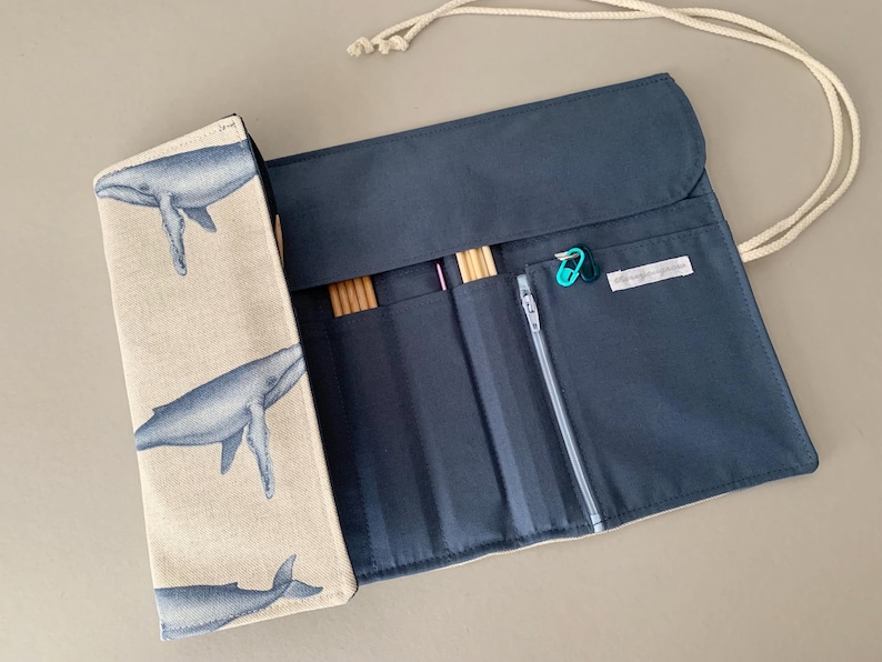 Puede incluir: Estuche para agujas de tejer azul marino con solapa beige estampada con ilustraciones de ballenas azules. El estuche est&aacute; abierto, revelando bolsillos y contenido. Incluye un bolsillo con cremallera y ranuras para agujas de tejer y accesorios. Se adjunta un cord&oacute;n blanco.