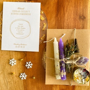 Puede incluir: Un sobre de papel marrón con una vela blanca y morada, un pequeño manojo de hierbas secas, un palo de incienso negro y un pequeño frasco de cristales. El sobre está atado con una cuerda y tiene una nota escrita a mano que dice "Ritual: Cerrar Ciclos y Nuevos Comienzos" y "Cerré mis ojos a viejos finales y los abri a nuevos comienzos".