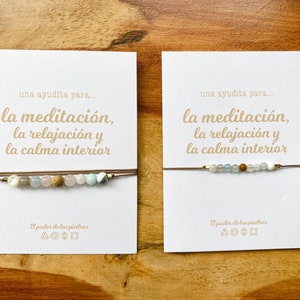Op de afbeelding: Twee kaarten met de tekst "una ayudita para... la meditaci&oacute;n, la relajaci&oacute;n y la calma interior" en een bruin koordarmband met verschillende gekleurde kralen.