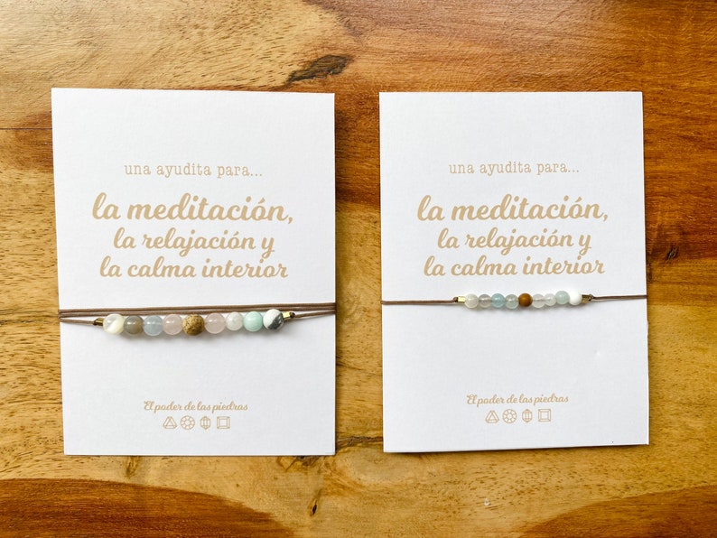 Op de afbeelding: Twee kaarten met de tekst "una ayudita para... la meditaci&oacute;n, la relajaci&oacute;n y la calma interior" en een bruin koordarmband met verschillende gekleurde kralen.