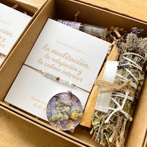 Op de afbeelding: Twee cadeaudozen met een meditatiethema. Elke doos bevat een kaart met de tekst "una ayudita para... la meditaci&oacute;n, la relajaci&oacute;n y la calma interior", een armband met kralen, een klein rond harsstuk met gedroogde bloemen en een kristal, en een wierookstokje met gedroogde kruiden en een wit kristal.