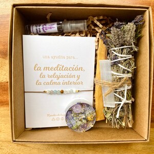 Op de afbeelding: Een bruine doos met een witte kaart met de tekst "una ayudita para... la meditaci&oacute;n, la relajaci&oacute;n y la calma interior", een klein flesje lavendelolie, een wierookstokje, een helder kristal en een armband met kralen.