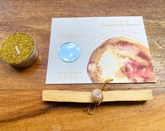 May include: A gold glitter tea light candle, a card with a circular mirror, and a bundle of Palo Santo wood tied with a stone and string. The card has text in Spanish: "21 de junio Solsticio de Verano".