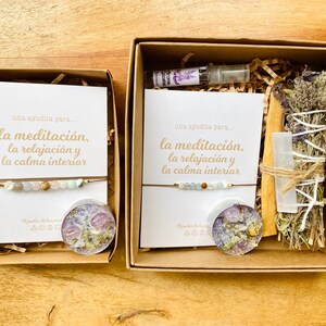 Op de afbeelding: Twee bruine cadeaudozen met open deksels. De dozen bevatten items voor meditatie en ontspanning. De linker doos bevat een armband, een kaars en een kaart met de tekst "una ayudita para... la meditaci&oacute;n, la relajaci&oacute;n y la calma interior". De rechter doos bevat een wierookstokje, een kristal, een flesje etherische olie en een kaart met de tekst "una ayudita para... la meditaci&oacute;n, la relajaci&oacute;n y la calma interior".