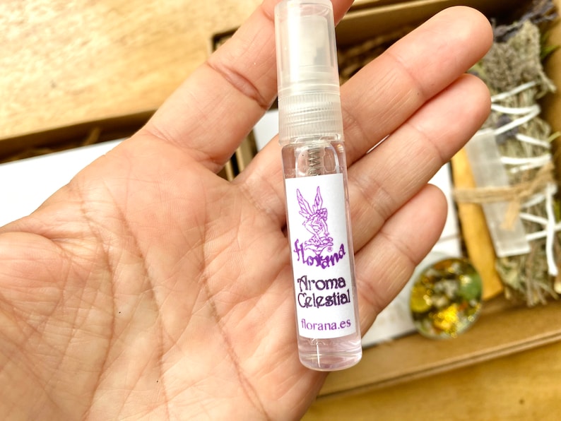 Op de afbeelding: Een doorzichtige glazen fles met een paars label waarop "Florana Aroma Celestial" en "florana.es" staat. De fles is in de hand van iemand.