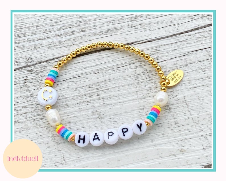 May include: A gold bracelet with white beads and colorful beads that spell out "HAPPY". The bracelet also has a small gold charm with the text "Wunder  bl&uuml;hen  sch&ouml;n".