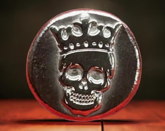 May include: A silver coin with a skull wearing a crown. The coin has a red background.