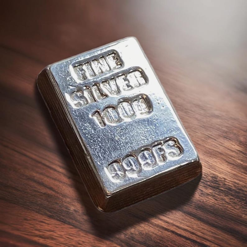Pode incluir: Uma barra de prata com as palavras "FINE SILVER 1000 999FS" gravadas nela.