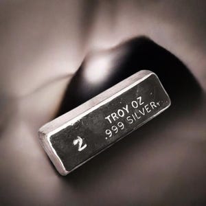 May include: A silver bar with the text "2 Troy oz .999 Silver" engraved on it.