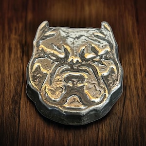 May include: A silver-colored metal pendant shaped like a bulldog's head. The pendant has a detailed, textured design and a realistic expression.