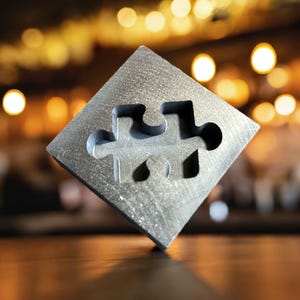 May include: A silver metal puzzle piece shaped like a puzzle piece. The puzzle piece is sitting on a wooden surface.