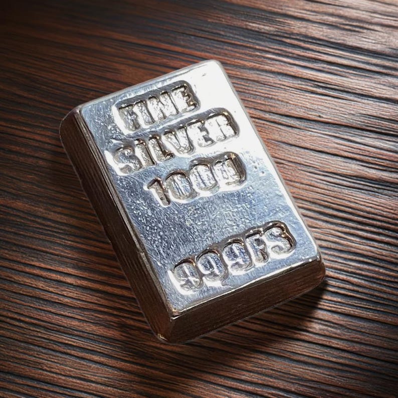 Pode incluir: Uma barra de prata com as palavras "FINE SILVER 1000g 999.9FS" gravadas em relevo.