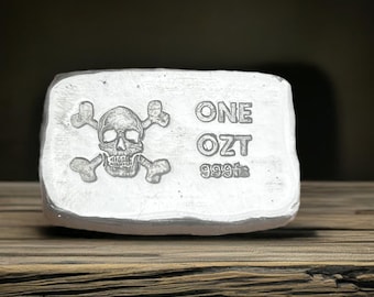Könnte beinhalten: Ein Silberbarren mit einem Totenkopf- und Knochenkreuz-Design und dem Text "ONE OZT 999.9" darauf.