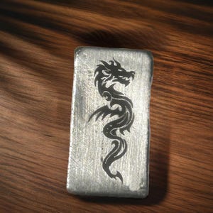 May include: A silver metal bar with a black dragon design engraved on the front.