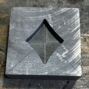 May include: A gray, rectangular mold with a diamond-shaped cutout. The mold has a textured surface and is made of a durable material.