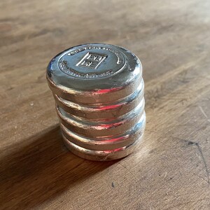 Puede incluir: Una pila de cuatro pesas de metal de color plateado con el texto "1 KG FINE SILVER 999" en la pesa superior.