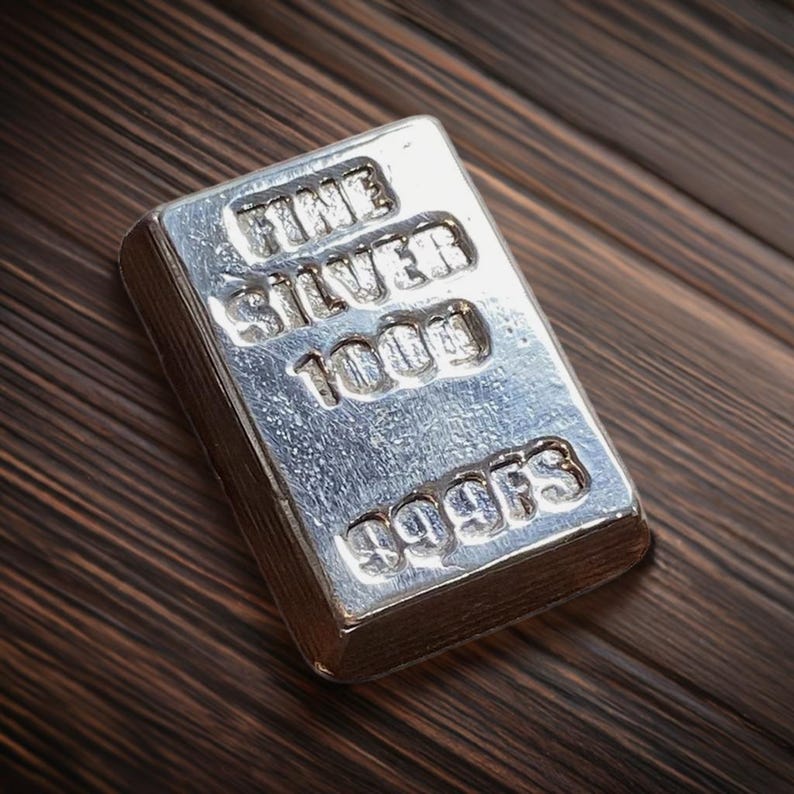 Pode incluir: Uma barra de prata com as palavras "FINE SILVER 1000" e "999FS" gravadas nela.